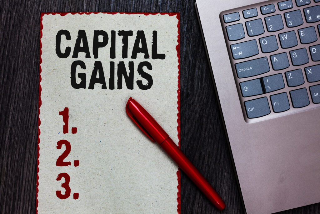 Handwriting text writing Capital Gains. Concept meaning Bonds Shares Stocks Profit Income Tax Investment Funds Piece paper red borders black marker computer keyboard wooden background.