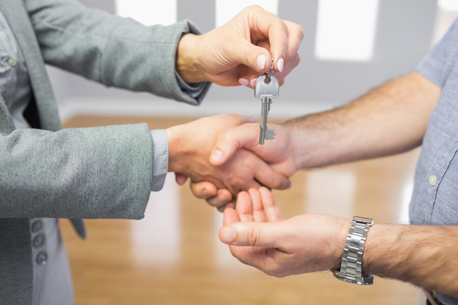 Two people shaking hands in front of a house.