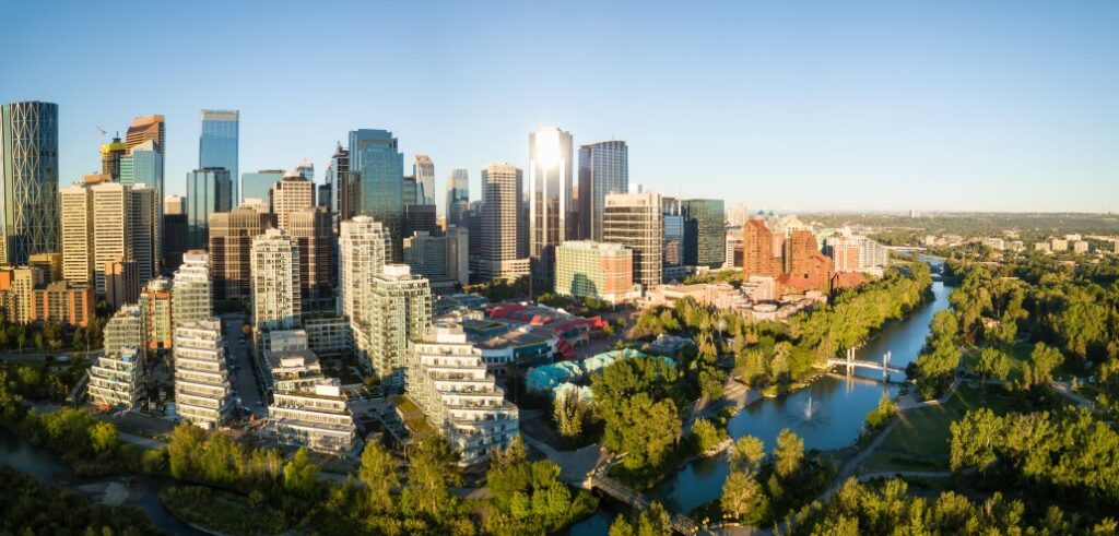 Aerial view of a city skyline with modern skyscrapers and green spaces, adjacent to a winding river and bridges under a clear blue sky.