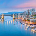 The city of vancouver at dusk with boats docked in the harbor.