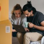 couple-surrounded-by-boxes-checks-laptop-details-on-moving-day