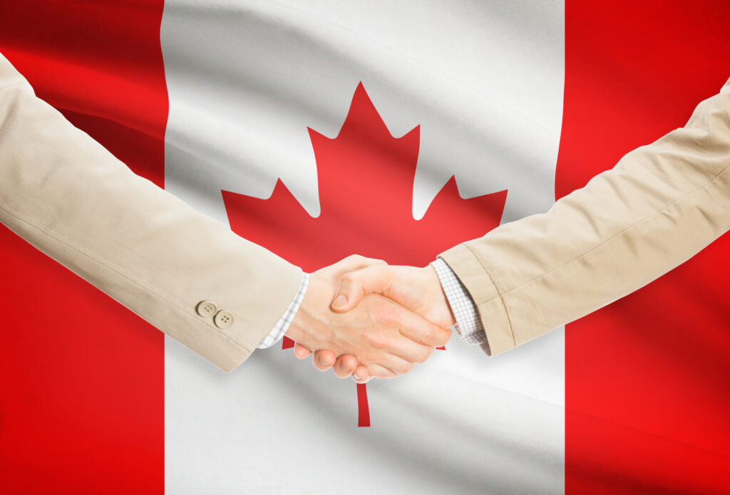 Two businessmen shaking hands in front of a canadian flag.