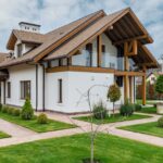 exterior-of-modern-cottage-house-with-columns-and-balcony-surrounded-by-green-grass-and-trees