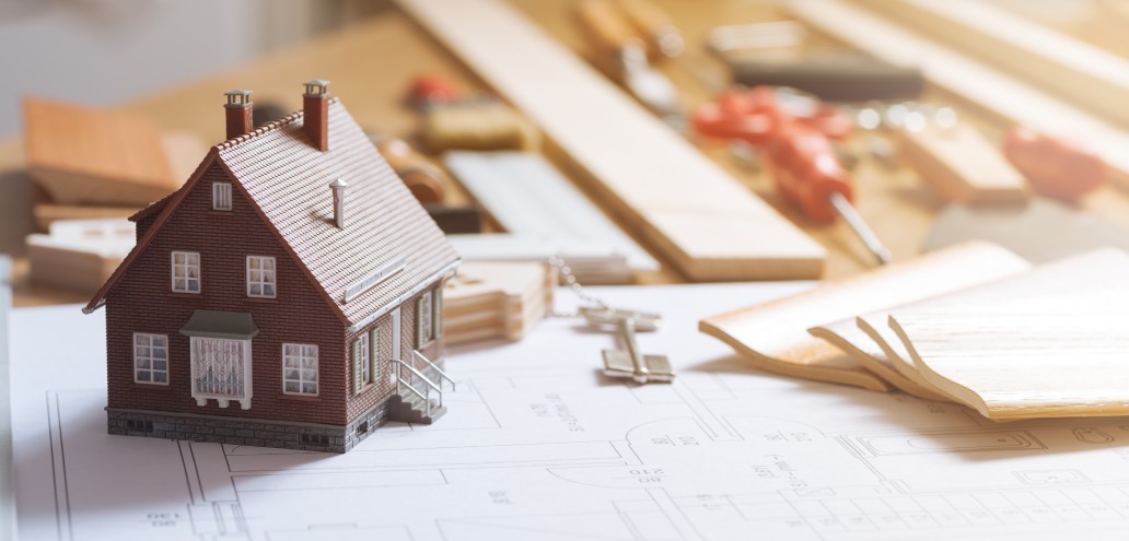 A model house sits on top of blueprints and tools.