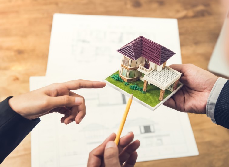 Two people holding a model of a property on a table.