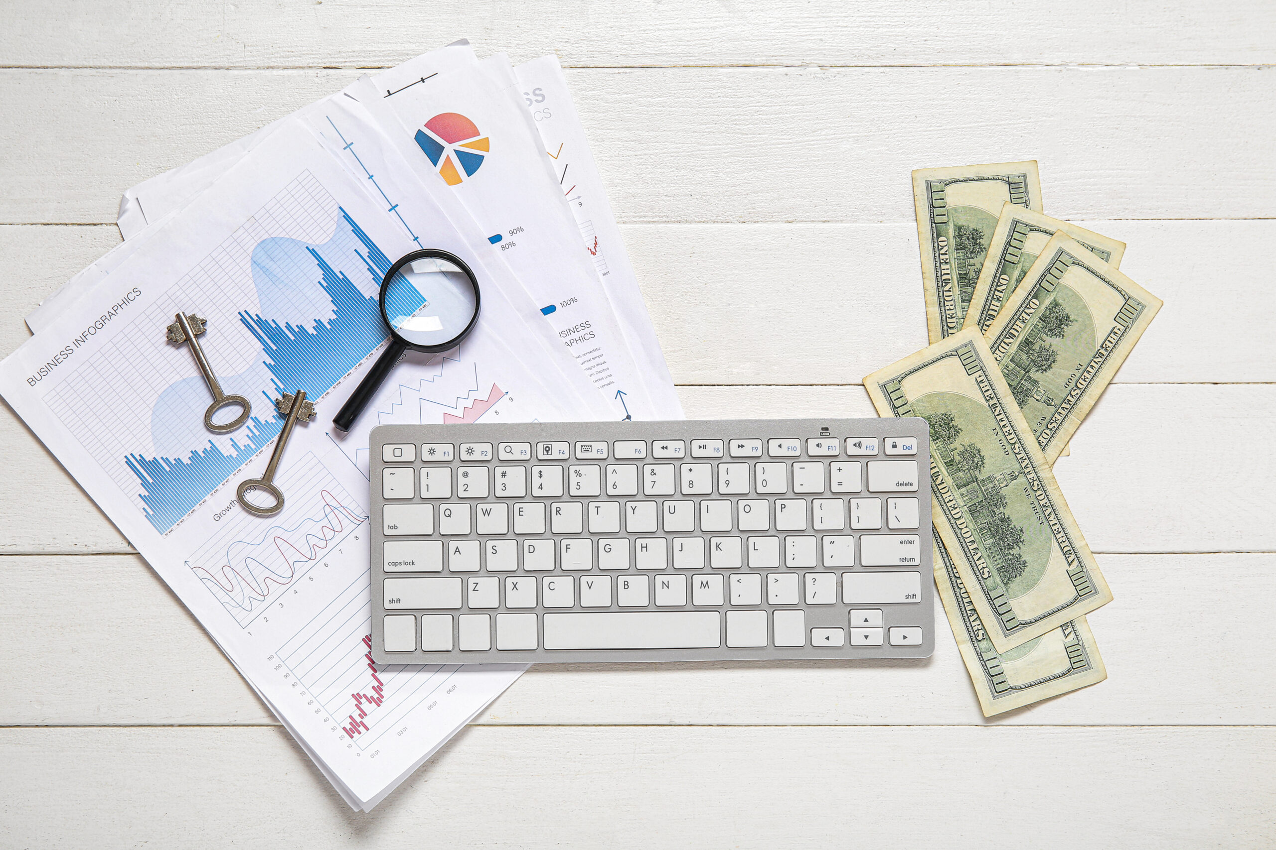 Keyboard with diagrams, keys, magnifier and money on white woode