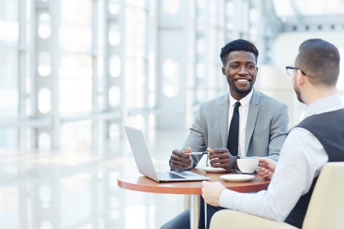 Two businessmen sitting at a table and talking to each other.