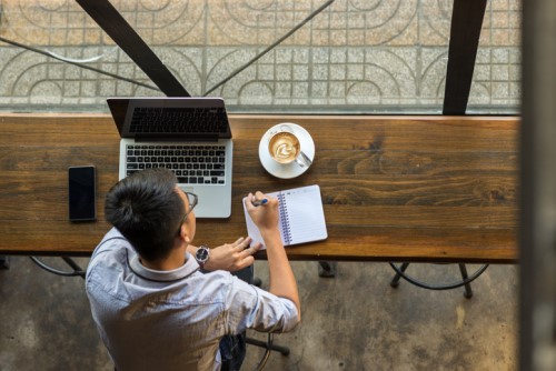 A man sitting at a table with a laptop and a cup of coffee.