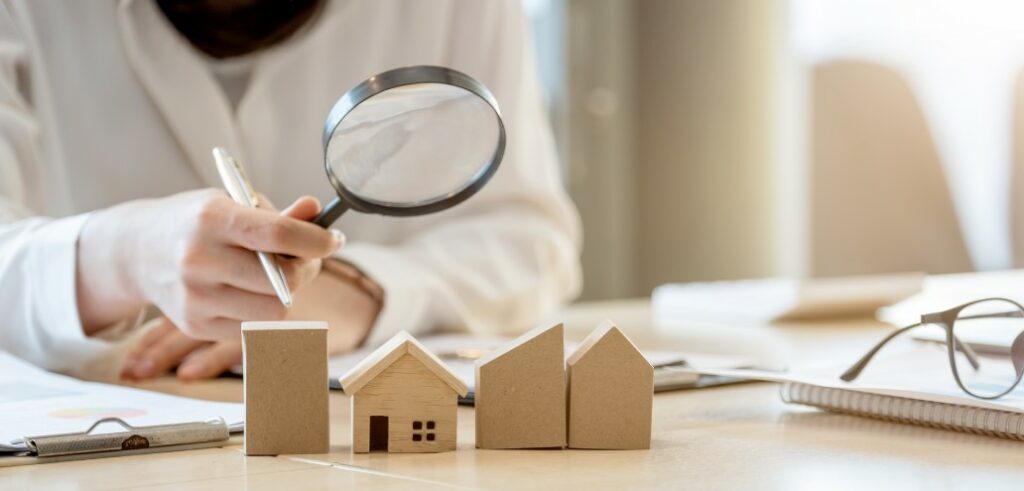 A woman is examining a model of a property with a magnifying glass.