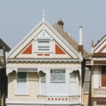 Three adjoining Victorian-style houses with ornate trim, each painted in different pastel colors. The houses have pointed roofs and large front windows.