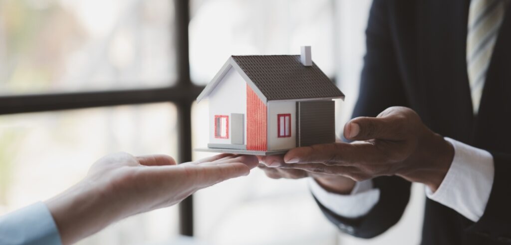 A man handing a model house to a woman in a business suit.