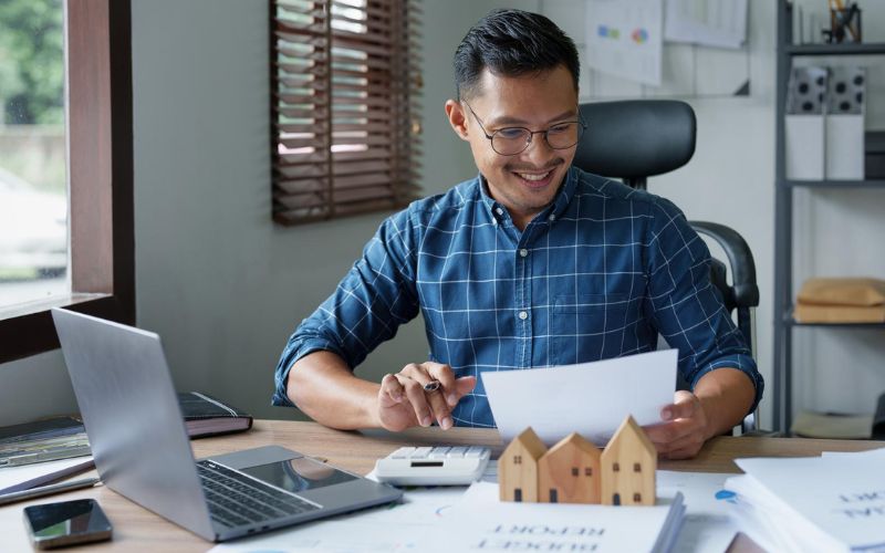 Asian businessman looking at a house model at his desk.