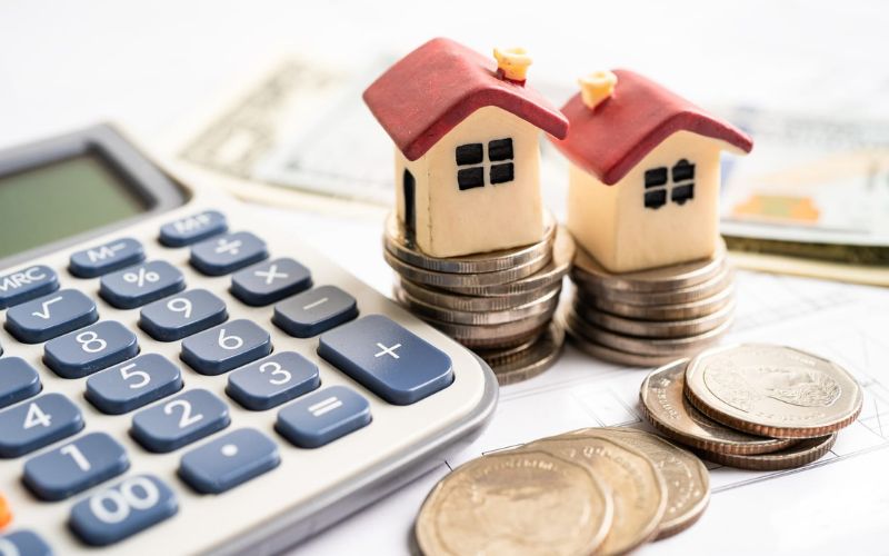 A stack of house models and a calculator on top of a pile of money.