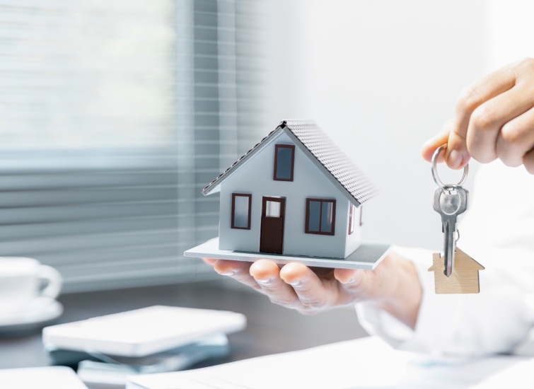 A woman holding a model house with keys in her hand.