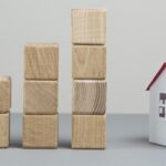 Four stacks of wooden blocks arranged in ascending order next to a small model house with a red roof, symbolizing the gradual steps toward securing a mortgage.