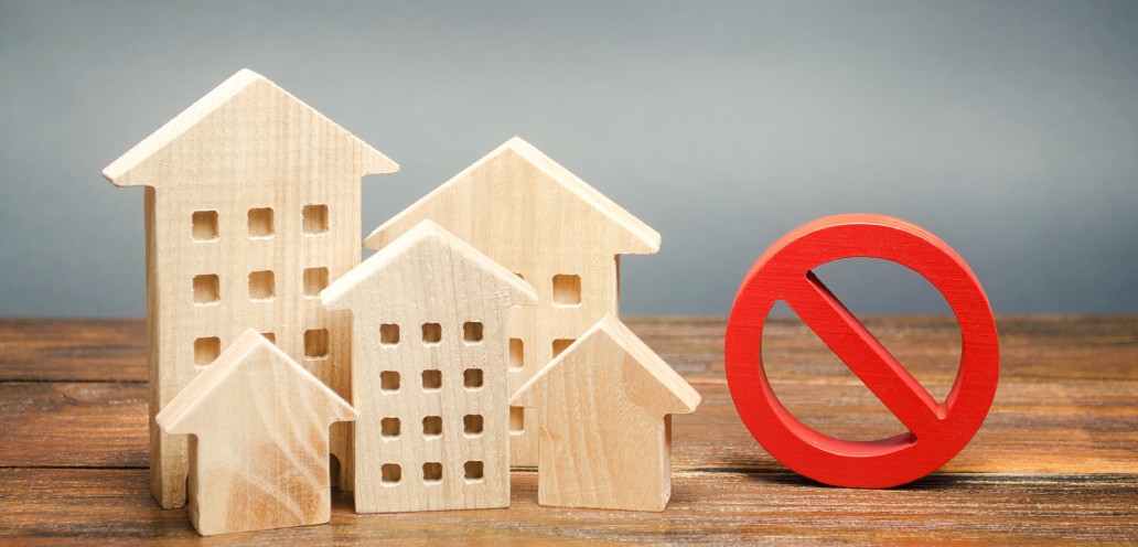 A wooden model of a house with a red no sign next to it.